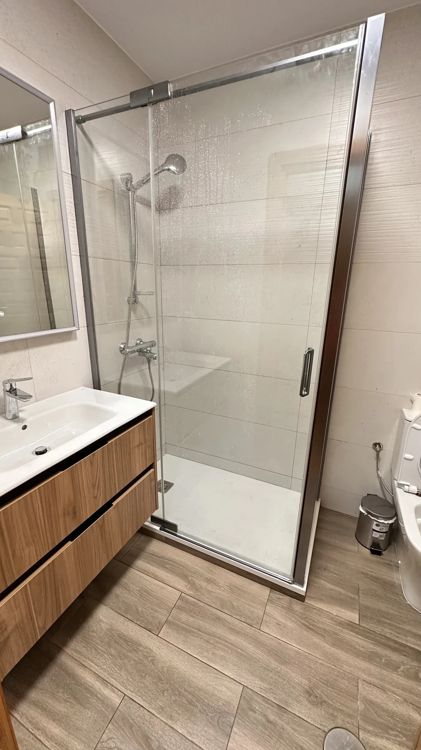 Baño reformado con mueble de lavabo en madera, mampara de ducha de cristal y suelo porcelánico efecto madera