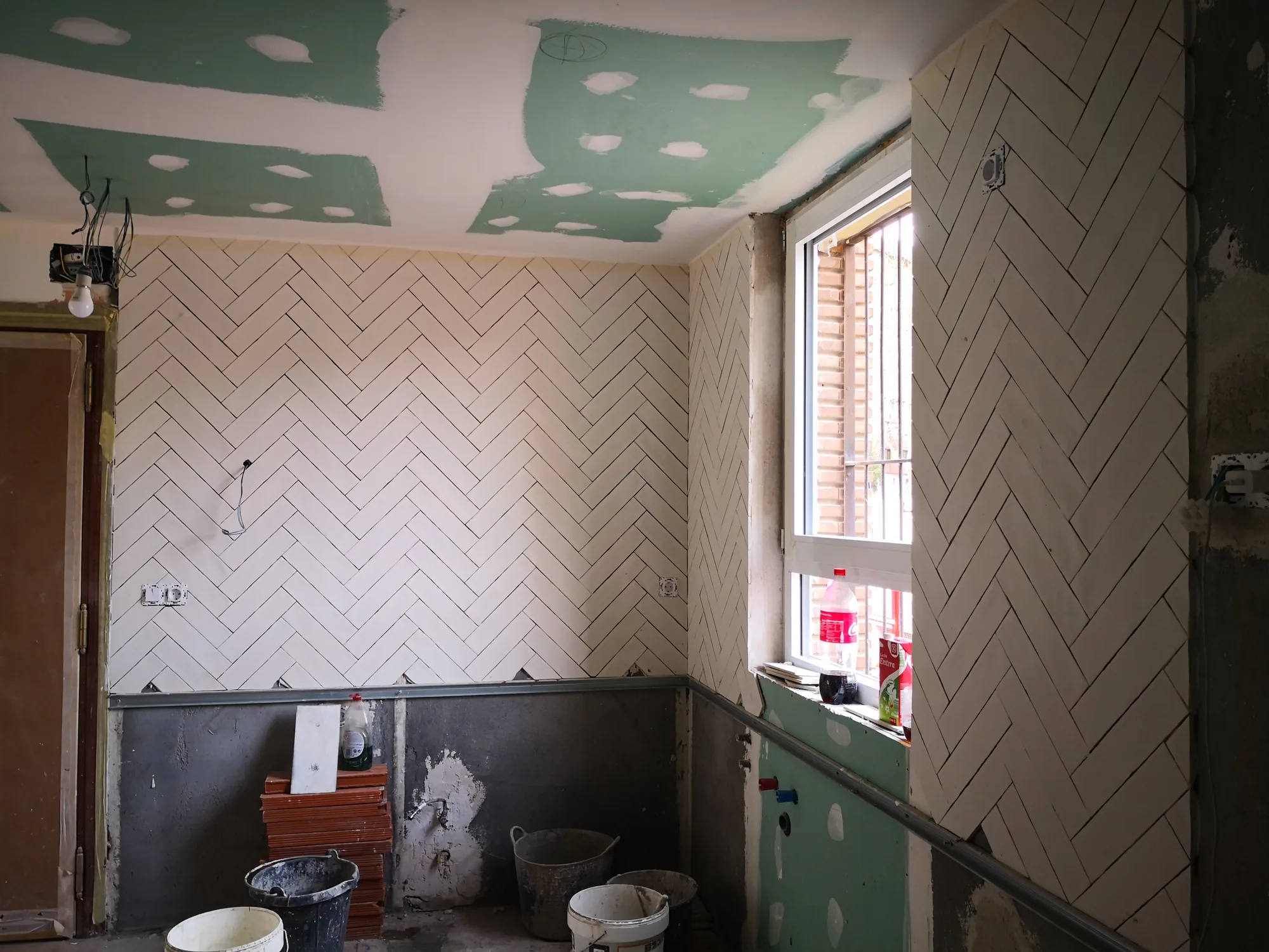 Cocina en obra con alicatado en espiga recién colocado, techo de pladur sin pintar y cubos de material en el suelo